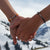 Händchenhaltend ANKERLIFT Armbänder in beiden Farben orange und schwarz vor schneebedeckten Bergen im Skigebiet