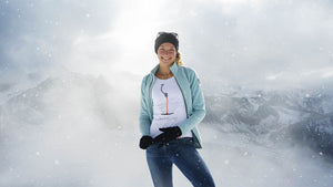 Model trägt weißes ANKERLIFT T-Shirt vor schneebedeckten Bergen im Skigebiet bei sonnigem Wetter.