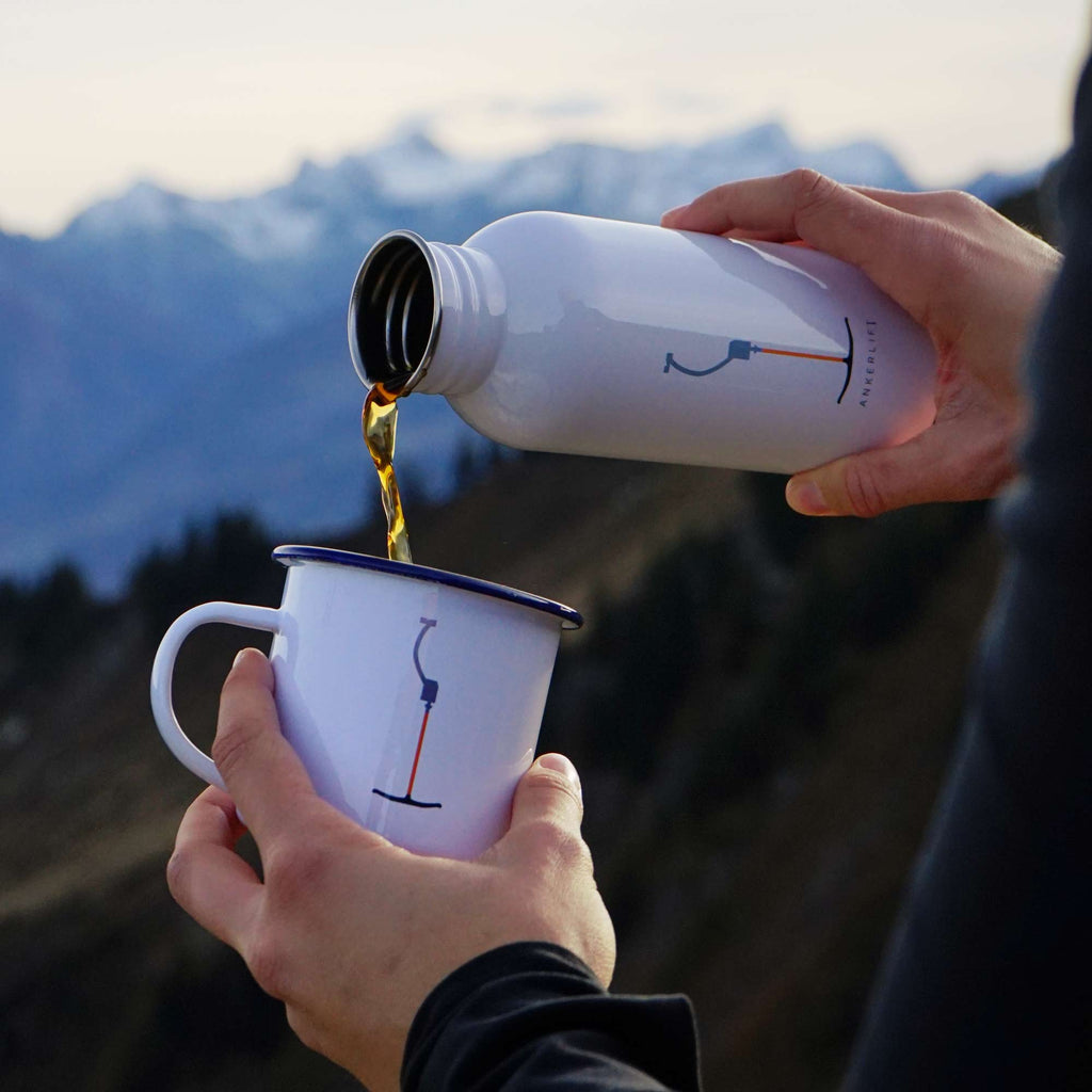Eine weiße "ANKERLIFT" Emaille Tasse von ANKERLIFT vor Bergpanorama